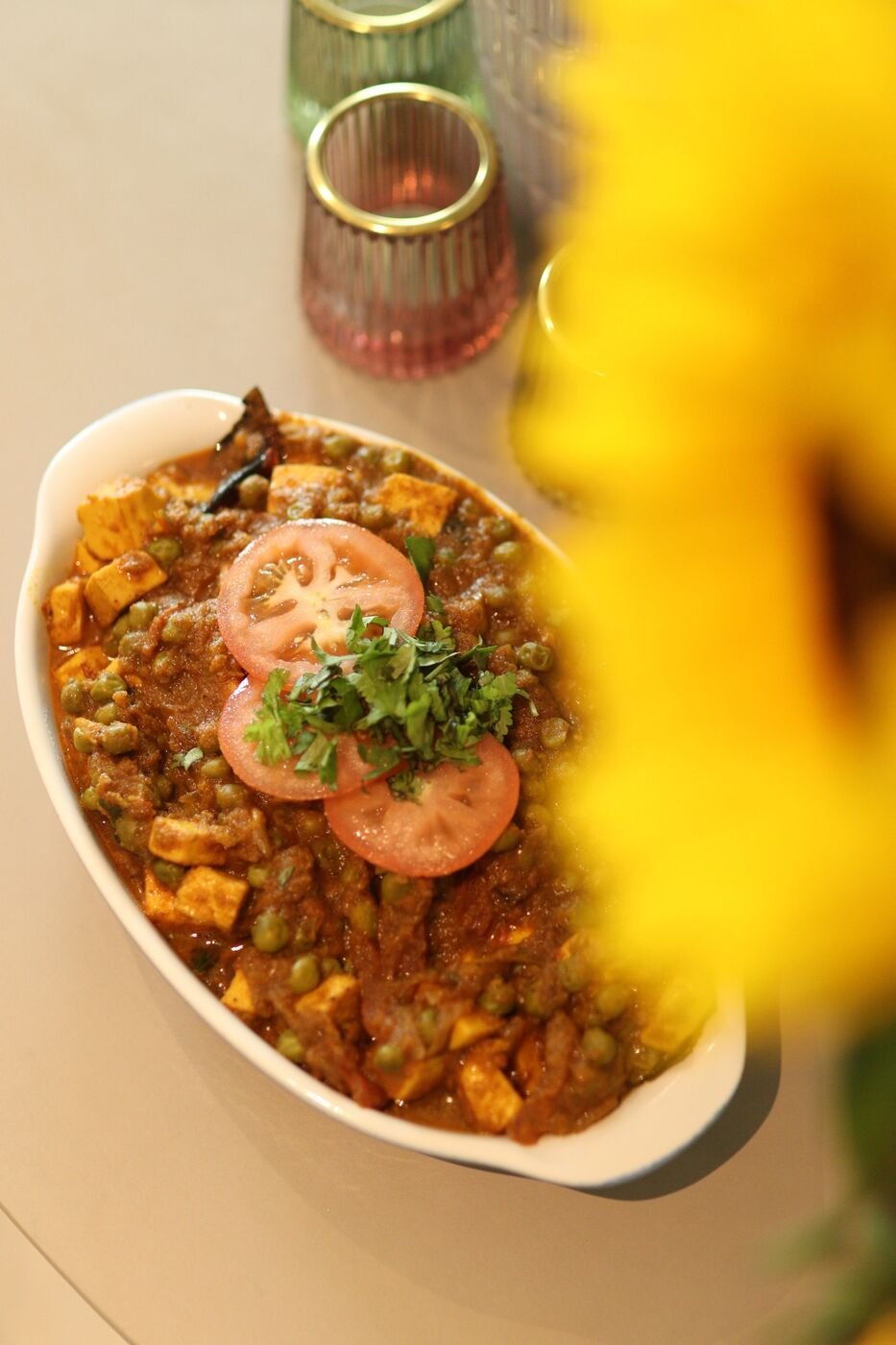Matar paneer garnished with tomato and coriander beside a yellow flower, Eccentric Food Tales
