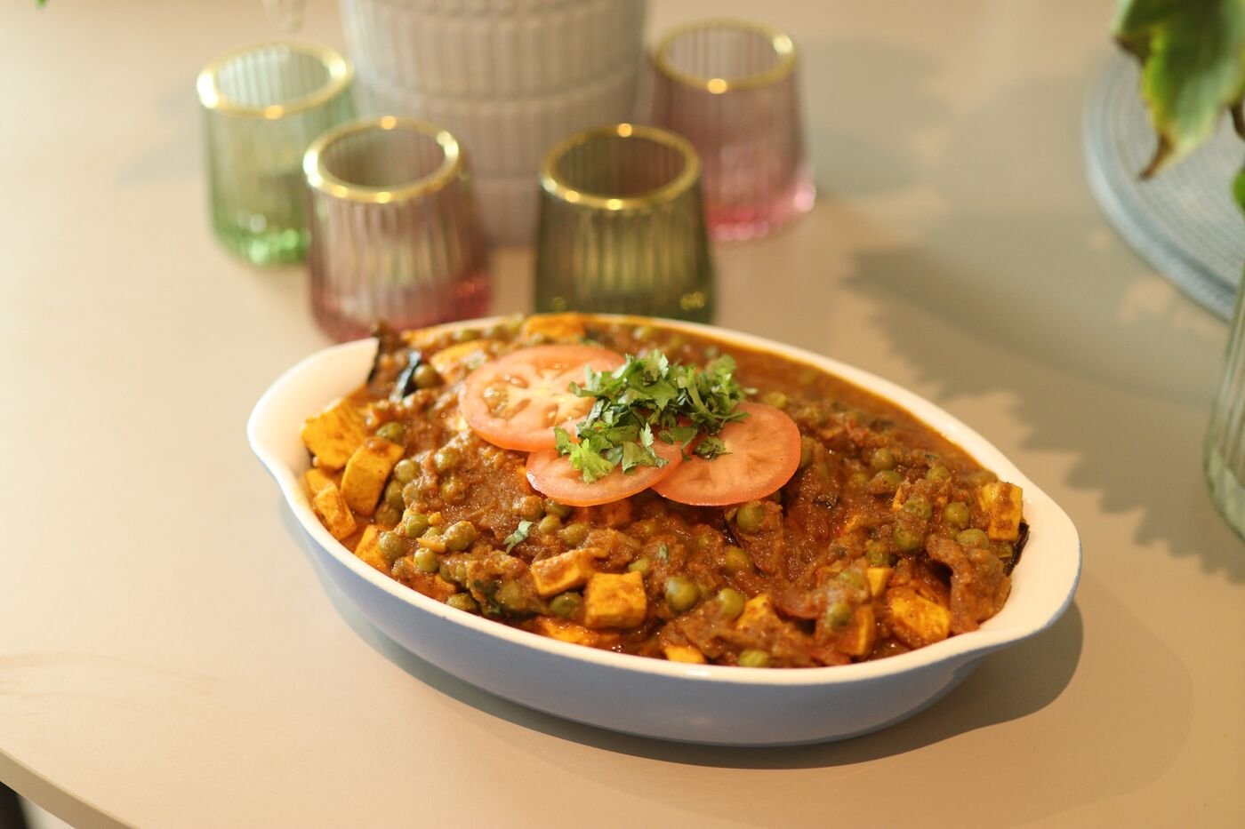 Matar paneer in an oval dish with coloured glass candle holders, Eccentric Food Tales