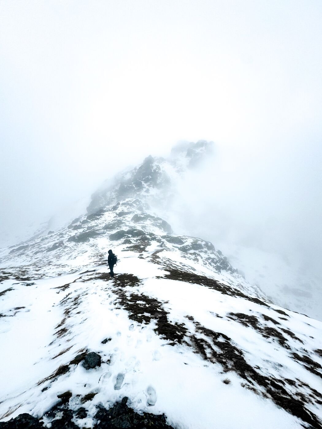 Hiker silhouetted on a snowy ridge in the Scottish Highlands in winter