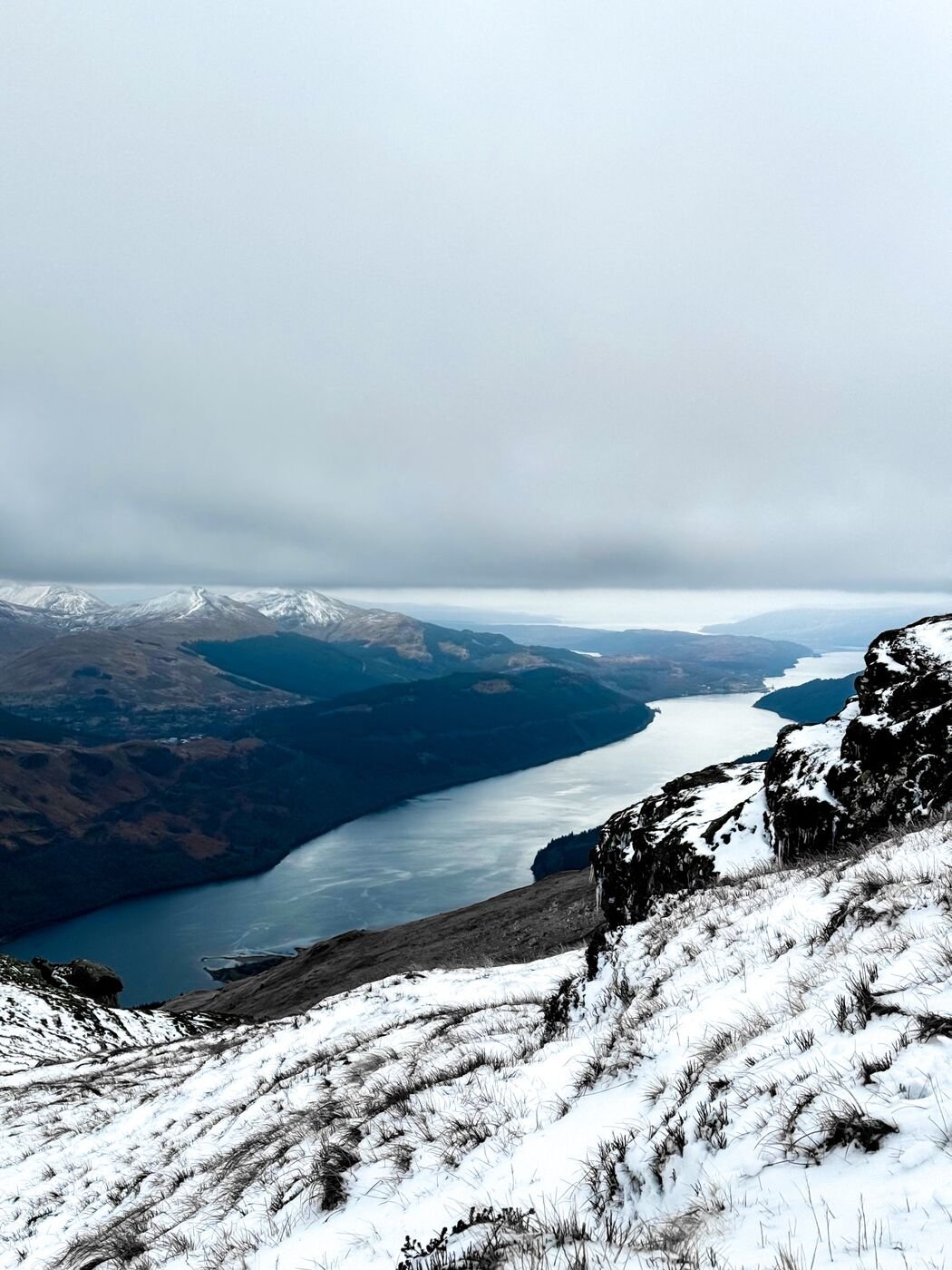 Snow covered hills rising above a dark loch in the Scottish Highlands